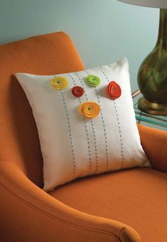 a pillow with buttons on it sitting on a chair next to a vase and lamp