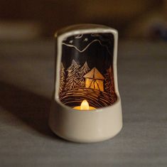 a small candle holder with a camp scene on it's side and a lit candle in the middle