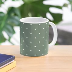 a green and white polka dot mug sitting on top of a wooden table next to a book