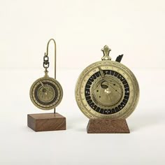 an antique pocket watch and earring stand on a wooden block with a white background