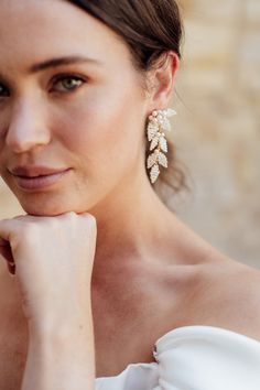 a woman in a white dress is posing with her hand on her chin and wearing large earrings