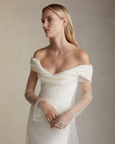 a woman in a white wedding dress with sheer sleeves on her shoulder and veil over her head