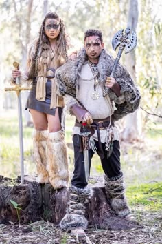 a man and woman dressed up as native americans in the woods with axes, swords and feathers