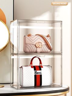 three clear shelves with purses and handbags in them on a table next to a mirror