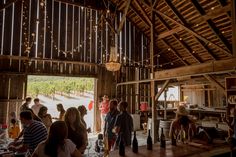 a group of people sitting at tables in a barn with lights hanging from the ceiling