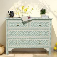 a white and blue dresser sitting next to a vase with flowers on top of it