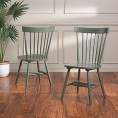 two green chairs sitting on top of a wooden floor next to a potted plant