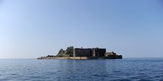 an island in the middle of the ocean with a building on it's side