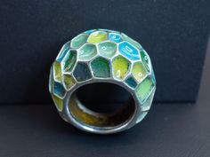 A gorgeous enameled silver statement ring in a size 7 1/2. Featuring a beautiful selection of blue and green enamel colors with a lovely emerald hidden on the back of the ring for the wearer to admire. Unique Green Patina Jewelry, Unique Green Jewelry With Patina, Modernist Green Ring For Gift, Green Modernist Ring As A Gift, Green Modernist Ring As Gift, Modernist Green Ring As A Gift, Modernist Green Rings For Gift, Modern Green Round Dome Ring, Green Enamel Rings As A Gift