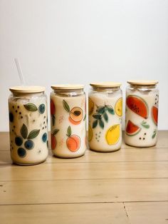 four jars with painted designs on them sitting on a wooden table next to each other