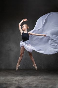 a young ballerina is in the air with her arms spread out and she is wearing a black tank top and white skirt