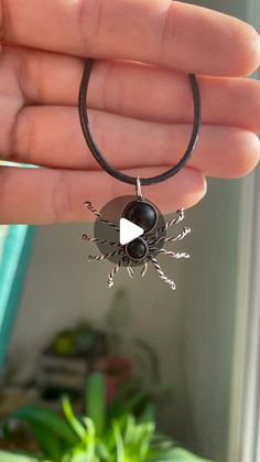 a hand holding a black and silver necklace with a spider on it's back