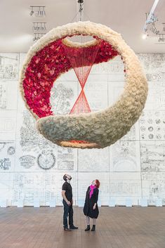 two people are standing in front of a large piece of art hanging from the ceiling