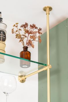 a glass shelf with flowers and wine glasses on it next to a wall mounted light