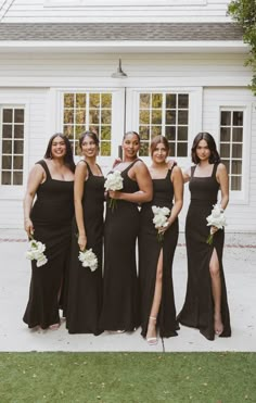 a group of women standing next to each other in front of a white building holding bouquets