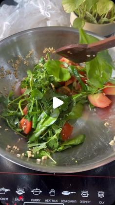 a metal bowl filled with greens and tomatoes