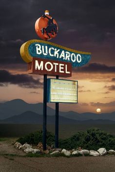 the sign for buckaroo motel is lit up at night with mountains in the background