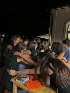 a group of people hugging each other in front of a window at night with the lights on