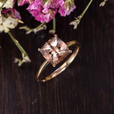 a pink diamond ring sitting on top of a wooden table next to purple and white flowers