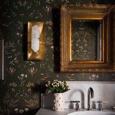 a bathroom sink under a mirror next to a wall paper with flowers and leaves on it