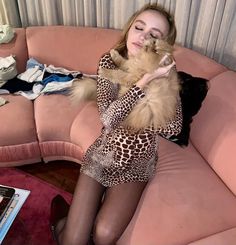 a woman sitting on a pink couch holding a brown cat in her hands and looking at the camera