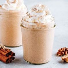 two jars filled with hot chocolate and whipped cream on top of a table next to cinnamons