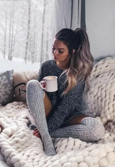 a woman sitting on top of a bed holding a cup of coffee