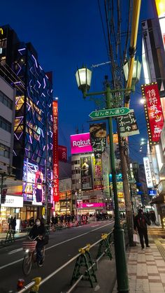 a city street at night with neon signs and people walking on the sidewalk in front of tall buildings