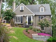 a gray house with white windows and black shutters in the front yard, surrounded by lush greenery