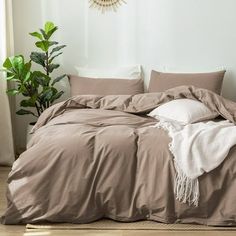 an unmade bed with pillows and blankets on it in a white room next to a potted plant