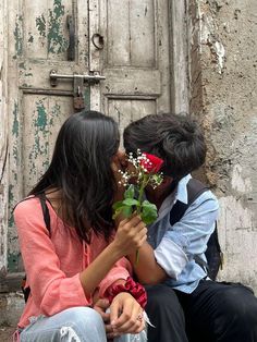 two people sitting next to each other with flowers in front of an old wooden door