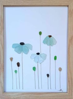 three white flowers with green stems in a wooden frame on a white wall and floor