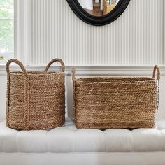 two woven baskets sitting on top of a white couch in front of a round mirror