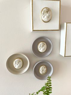 three white and gold plates sitting on top of a table next to a plant in a vase