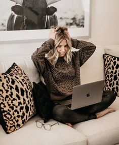 a woman sitting on a couch with her laptop in front of her face and wearing black leggings