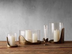 three candles are sitting on a wooden table next to two glass vases and one candle holder