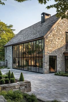 a large stone house with glass walls and windows on the front, surrounded by greenery