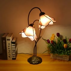 a lamp that is sitting on top of a table next to some books and flowers