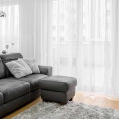 a gray couch sitting in front of a window next to a rug on top of a wooden floor