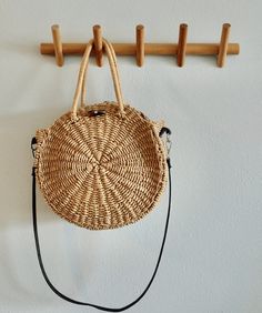 a wicker purse hanging from a wooden coat rack with hooks on the wall behind it