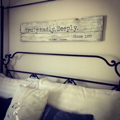 a bed with white pillows and a wooden sign above it that says truly madly deeply