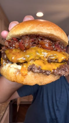 a man is holding up a cheeseburger with bacon and melted cheese on it