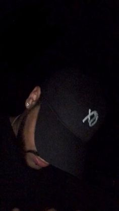 a man wearing a black hat and earring in the dark with his eyes closed