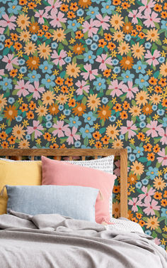 a bed topped with lots of pillows next to a wall covered in colorful floral wallpaper