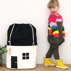 a little boy standing next to a bag with a house on it and a potted plant