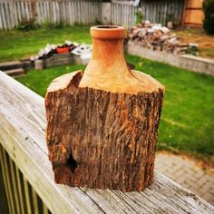 a wooden vase sitting on top of a wooden fence next to a green yard and grass