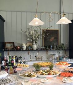 a kitchen counter topped with plates and bowls filled with food next to two hanging lights