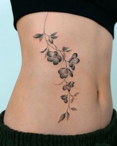 a woman's lower back tattoo with flowers and leaves on her side ribcage