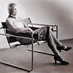 a woman is sitting in a chair with an open book on her lap and wearing a mask