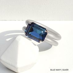 a blue stone ring sitting on top of a white rock in front of a white wall